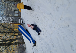 Chłopiec wbiega na górkę, a dziewczynka z niej zjeżdża na sankach