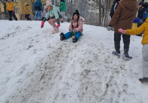 Dzieci na górce, dziewczynki przygotowują się do zjazdu z górki na sankach