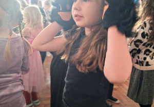 Dziewczynka w stroju czarnej kotki przykłada dłonie do uszu, naśladując kota