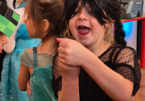 Dziewczynka w stroju bohaterki Wednesday śmieje się, kryjąc coś w raczkach