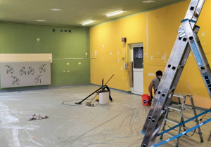 Sala przedszkolna w trakcie remontu z drabinami pośrodku, folią na podłodze i farbami na parapetach