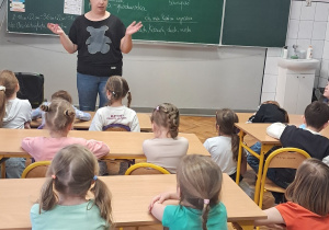 Dzieci w sali lekcyjnej słuchają, co mówi do nich pani