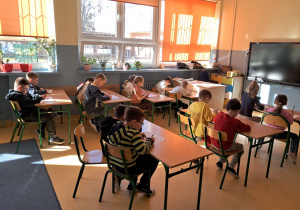Dzieci w ławkach w skupieniu wykonują zadania na kartce