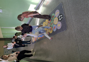 Dzieci na korytarzu szkolnym przeskakują po polach gry typu gra w klasy