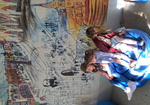 Dziewczynki odpoczywają na dużych pufach przed pomalowaną ścianą z widokami miasta Łodzi