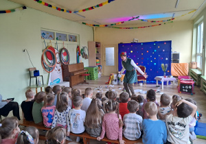 Aktor stojąc pośród rozsypanych śmieci zwraca się do dzieci siedzących na ławeczkach