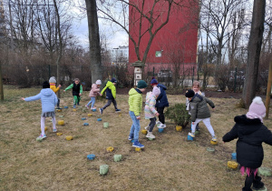 Dzieci roześmiane przeskakują po drewnianych słupkach