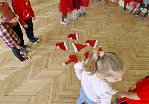 Dzieci stoją wokół rozłożonych na podłodze czerwonych czapeczek